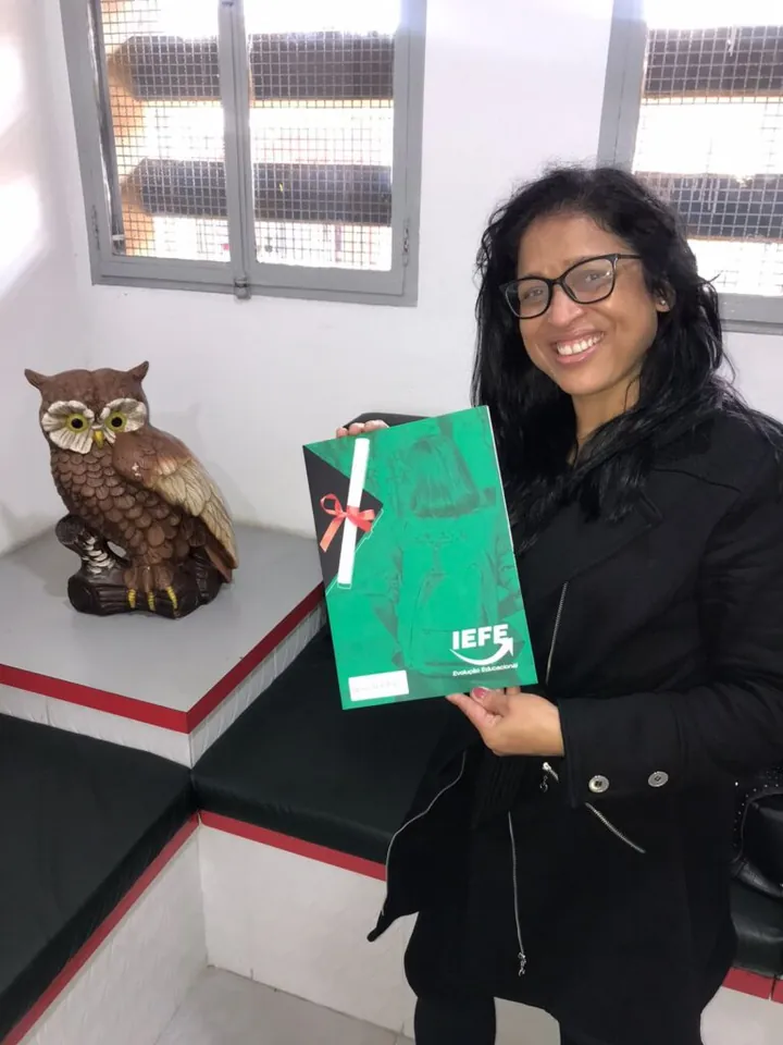 Aluna sorrindo com a pasta do diploma na sede